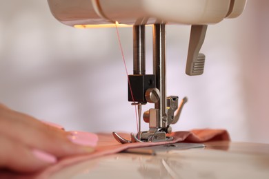 Photo of Woman working with sewing machine and fabric in workshop, closeup