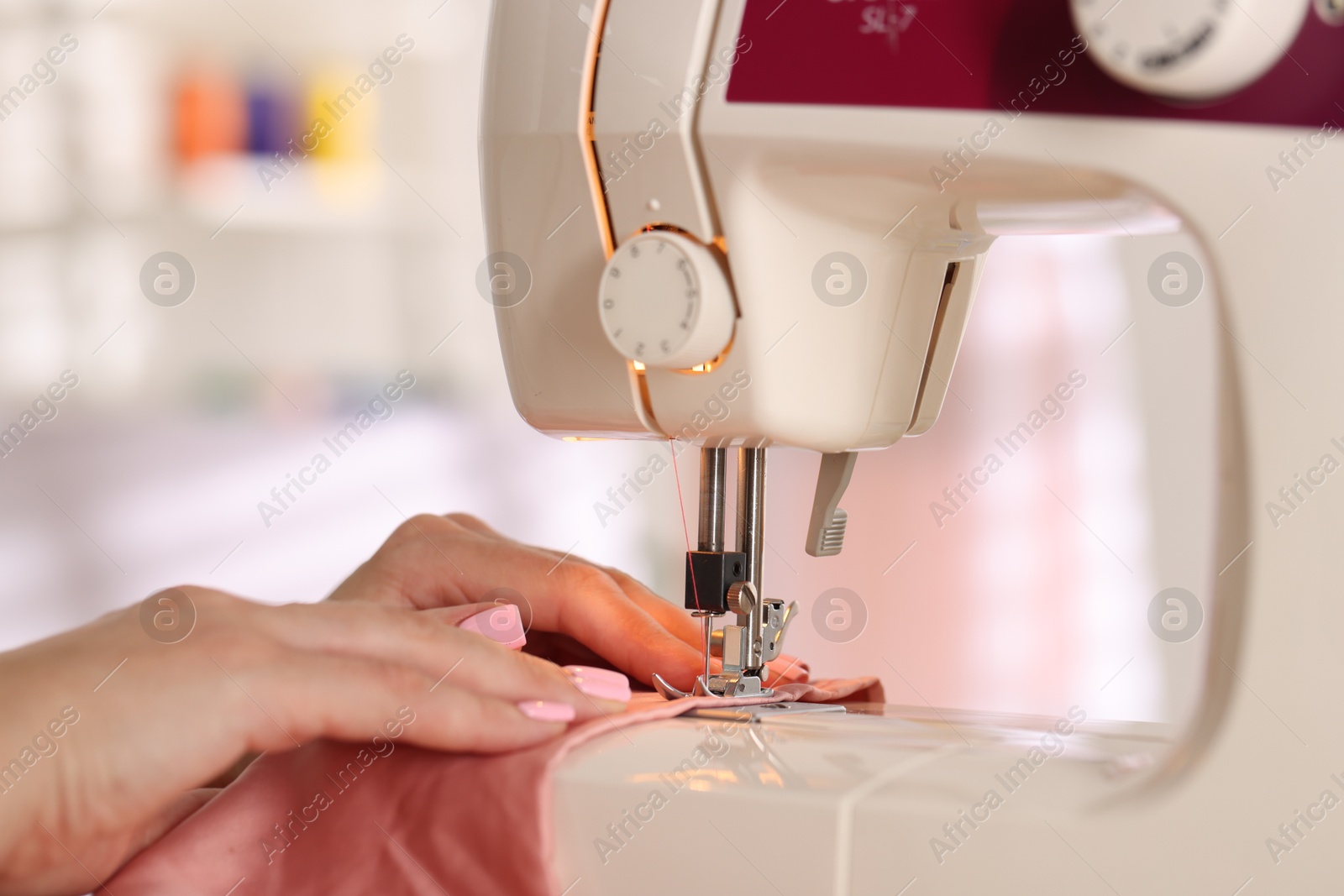 Photo of Woman working with sewing machine and fabric in workshop, closeup