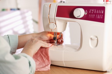 Photo of Woman working with sewing machine and fabric in workshop, closeup