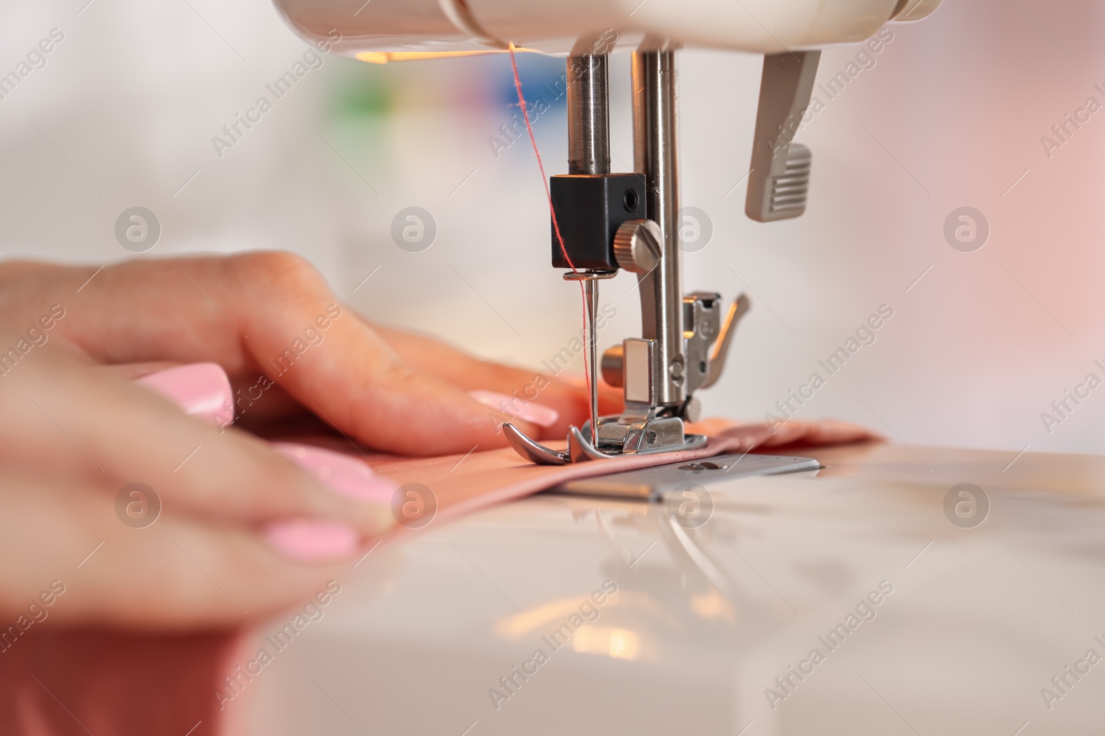 Photo of Woman working with sewing machine and fabric in workshop, closeup