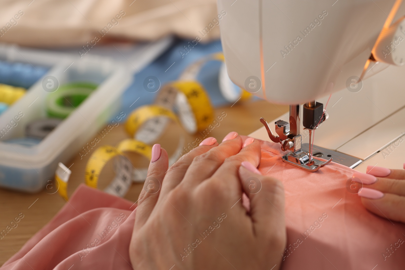 Photo of Woman working with sewing machine and fabric in workshop, closeup