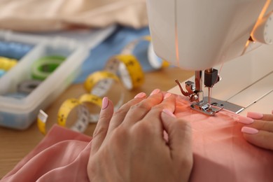 Photo of Woman working with sewing machine and fabric in workshop, closeup