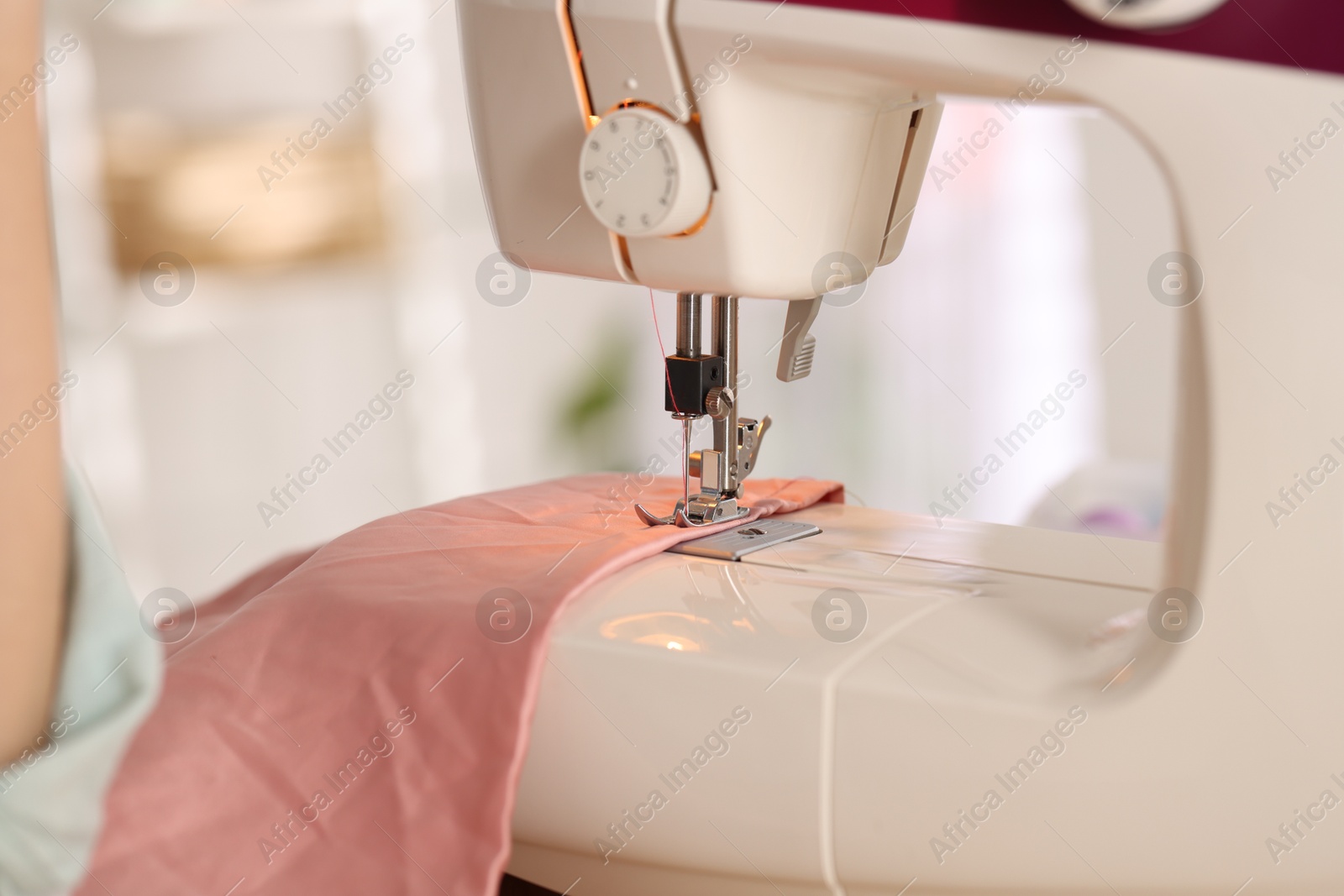 Photo of Closeup view of sewing machine with thread and pink fabric