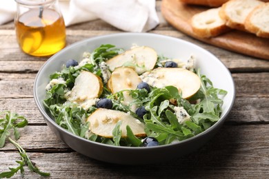 Photo of Tasty salad with arugula, pear, blue cheese, peanuts and blueberries in bowl on wooden table, closeup