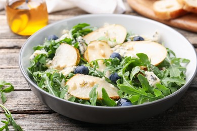 Photo of Tasty salad with arugula, pear, blue cheese, peanuts and blueberries in bowl on wooden table, closeup