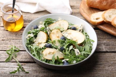 Photo of Tasty salad with arugula, pear, blue cheese, peanuts and blueberries in bowl on wooden table, closeup