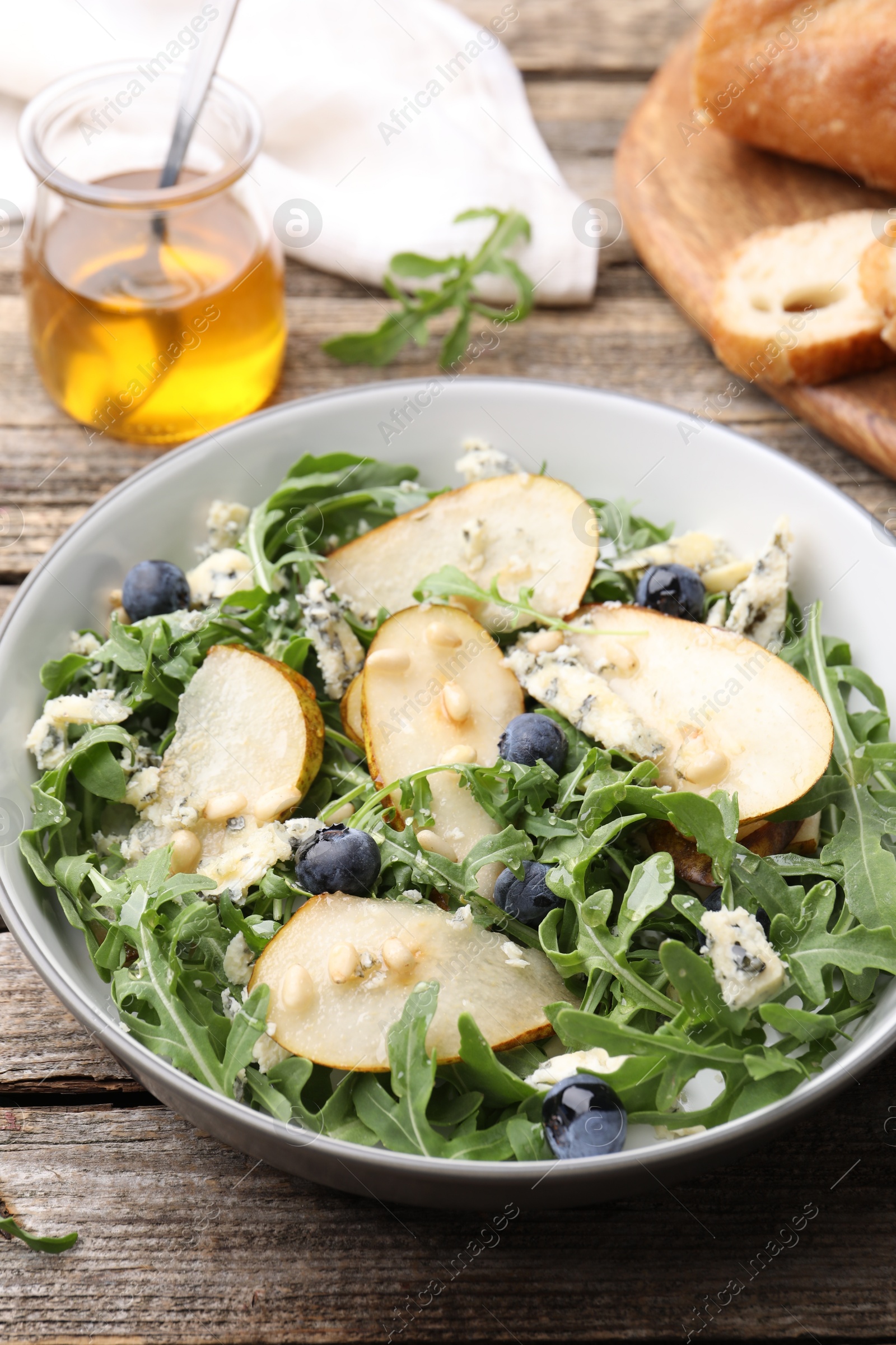Tasty salad with arugula, pear, blue cheese, peanuts and blueberries in bowl on wooden table, closeup Photo of Tasty salad with arugula, pear, blue cheese, peanuts and blueberries in bowl on wooden table, closeup