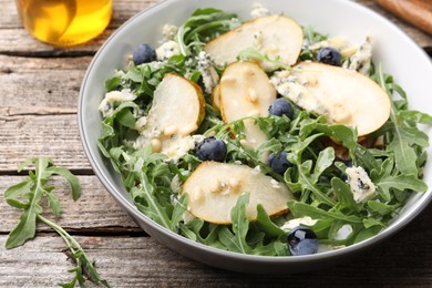 Photo of Tasty salad with arugula, pear, blue cheese, peanuts and blueberries in bowl on wooden table, closeup