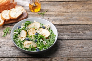 Photo of Tasty salad with arugula, pear, blue cheese, peanuts and blueberries in bowl on wooden table