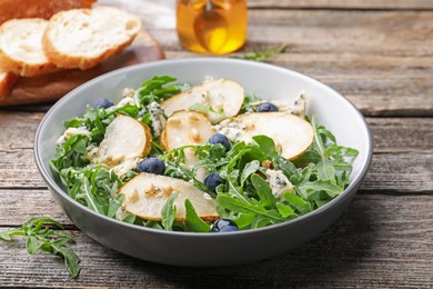 Photo of Tasty salad with arugula, pear, blue cheese, peanuts and blueberries in bowl on wooden table, closeup