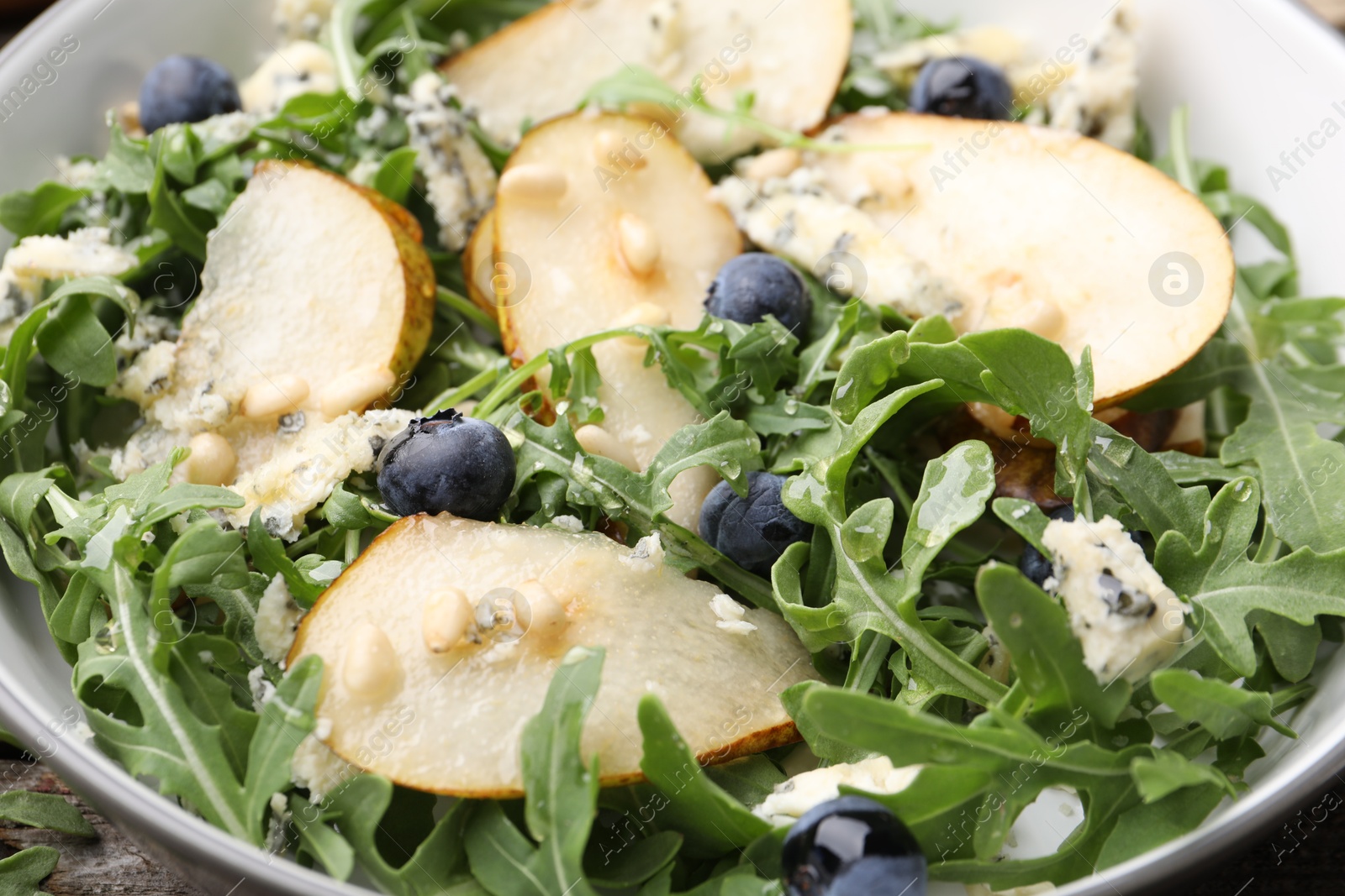 Tasty salad with arugula, pear, blue cheese, peanuts and blueberries in bowl on wooden table, closeup Photo of Tasty salad with arugula, pear, blue cheese, peanuts and blueberries in bowl on wooden table, closeup