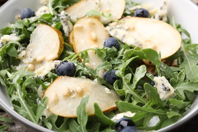Photo of Tasty salad with arugula, pear, blue cheese, peanuts and blueberries in bowl on wooden table, closeup