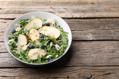 Photo of Tasty salad with arugula, pear, blue cheese, peanuts and blueberries in bowl on wooden table. Space for text