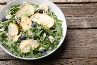 Photo of Tasty salad with arugula, pear, blue cheese, peanuts and blueberries in bowl on wooden table, above view. Space for text