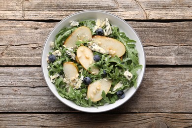 Photo of Tasty salad with arugula, pear, blue cheese, peanuts and blueberries in bowl on wooden table, top view