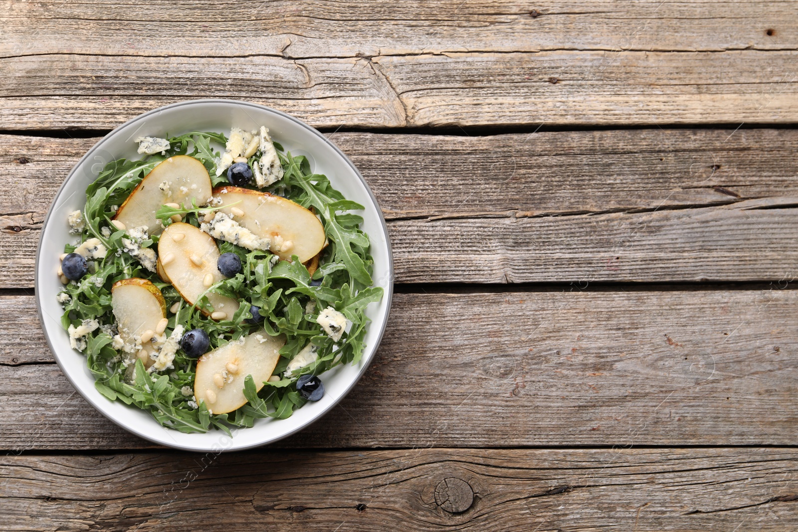 Tasty salad with arugula, pear, blue cheese, peanuts and blueberries in bowl on wooden table, top view. Space for text Photo of Tasty salad with arugula, pear, blue cheese, peanuts and blueberries in bowl on wooden table, top view. Space for text