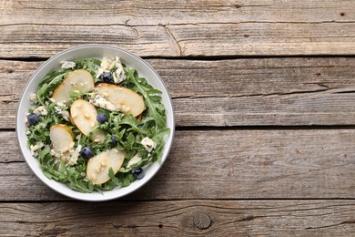 Photo of Tasty salad with arugula, pear, blue cheese, peanuts and blueberries in bowl on wooden table, top view. Space for text