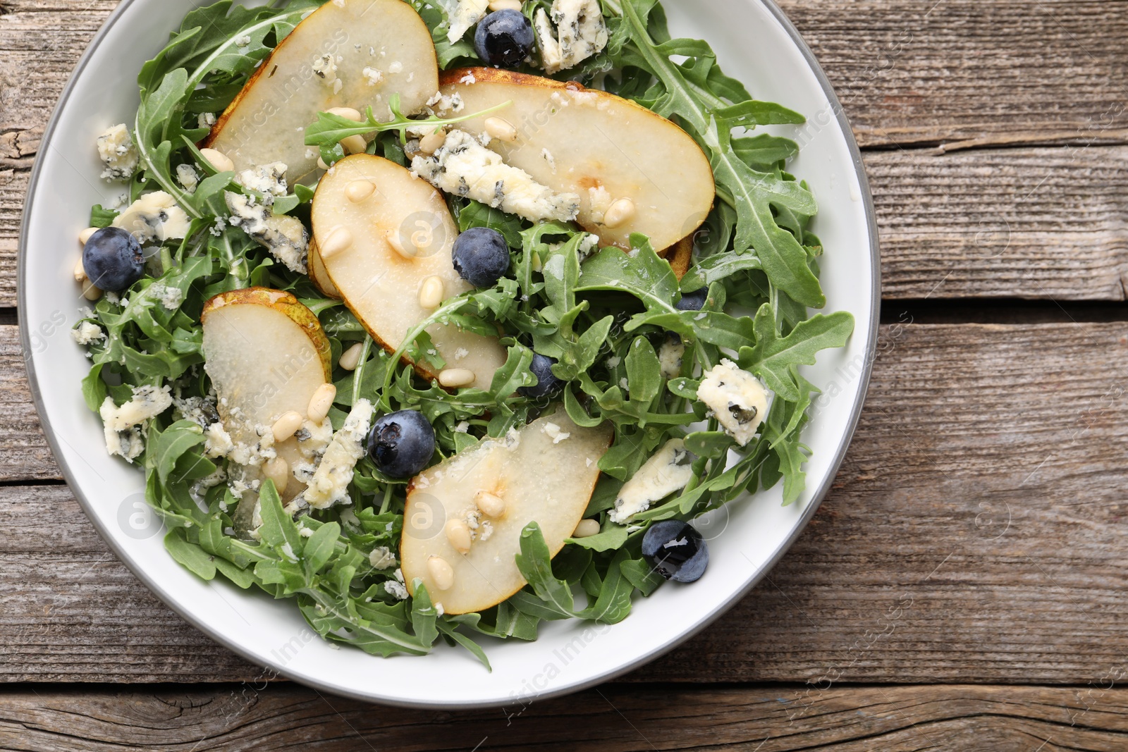 Tasty salad with arugula, pear, blue cheese, peanuts and blueberries in bowl on wooden table, top view Photo of Tasty salad with arugula, pear, blue cheese, peanuts and blueberries in bowl on wooden table, top view