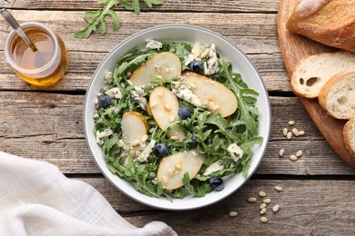 Photo of Tasty salad with arugula, pear, blue cheese, peanuts and blueberries in bowl on wooden table, flat lay