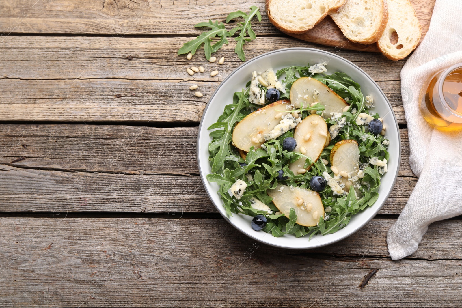Tasty salad with arugula, pear, blue cheese, peanuts and blueberries in bowl on wooden table, flat lay. Space for text Photo of Tasty salad with arugula, pear, blue cheese, peanuts and blueberries in bowl on wooden table, flat lay. Space for text