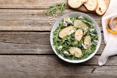 Photo of Tasty salad with arugula, pear, blue cheese, peanuts and blueberries in bowl on wooden table, flat lay. Space for text