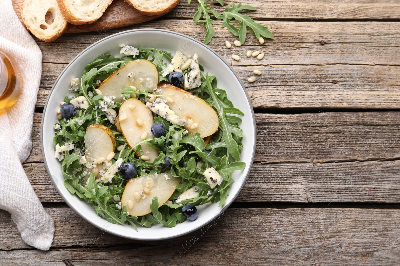 Tasty salad with arugula, pear, blue cheese, peanuts and blueberries in bowl on wooden table, flat lay. Space for text Photo of Tasty salad with arugula, pear, blue cheese, peanuts and blueberries in bowl on wooden table, flat lay. Space for text