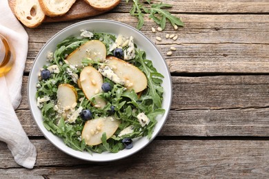 Photo of Tasty salad with arugula, pear, blue cheese, peanuts and blueberries in bowl on wooden table, flat lay. Space for text