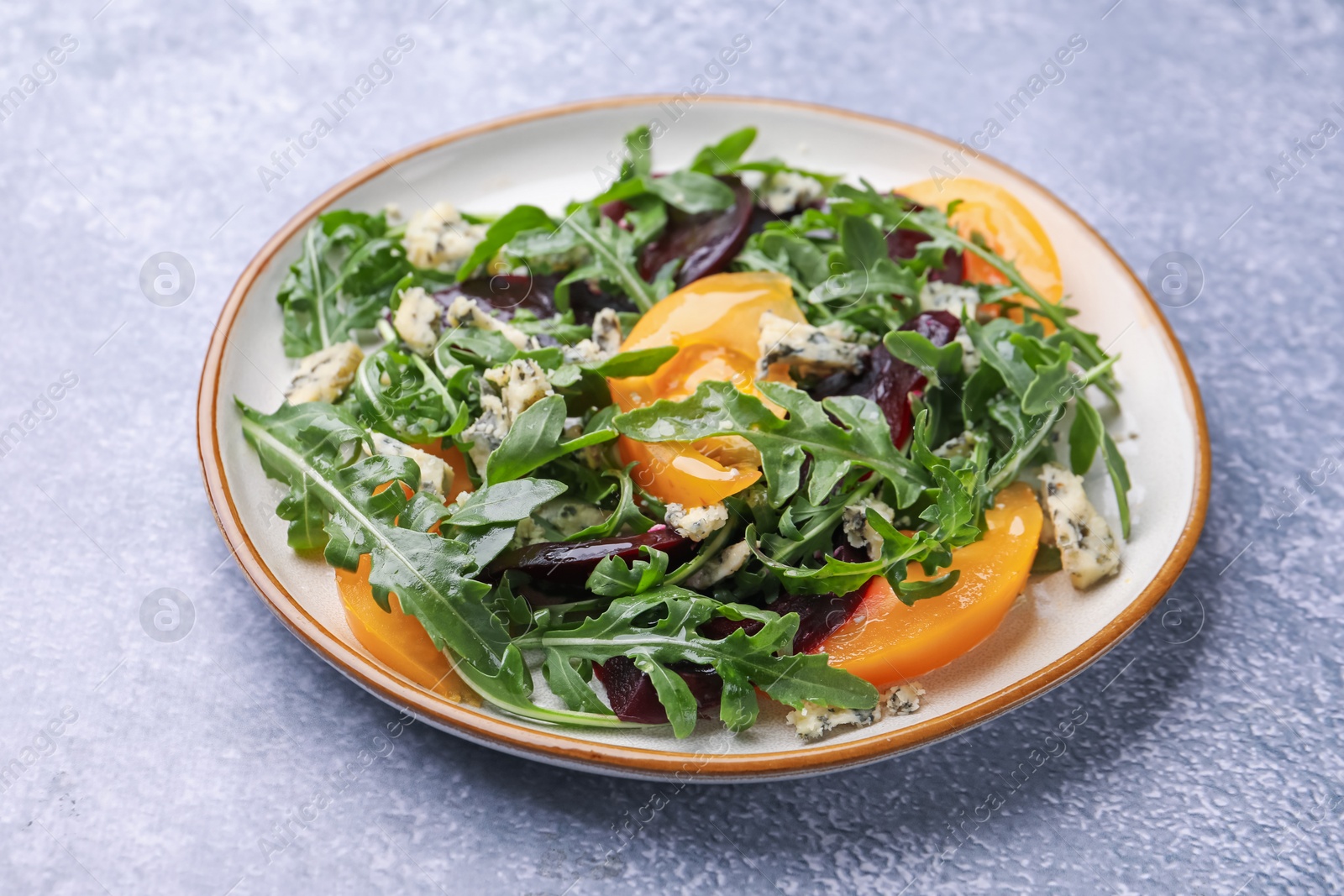 Tasty salad with arugula, blue cheese and vegetables on grey textured table, closeup Photo of Tasty salad with arugula, blue cheese and vegetables on grey textured table, closeup