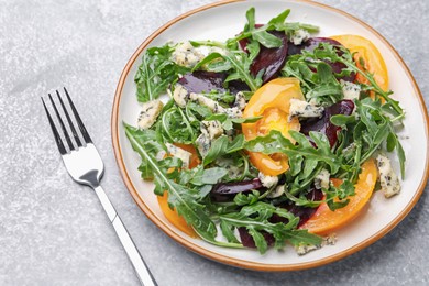 Photo of Tasty salad with arugula, blue cheese and vegetables on grey textured table, closeup