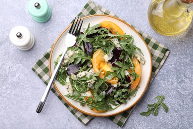 Photo of Tasty salad with arugula, blue cheese and vegetables on grey textured table, flat lay