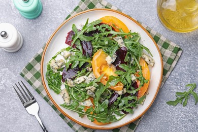 Photo of Tasty salad with arugula, blue cheese and vegetables on grey textured table, flat lay