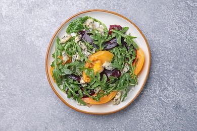 Photo of Tasty salad with arugula, blue cheese and vegetables on grey textured table, top view