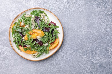 Photo of Tasty salad with arugula, blue cheese and vegetables on grey textured table, top view. Space for text
