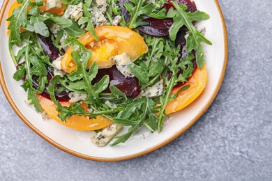 Photo of Tasty salad with arugula, blue cheese and vegetables on grey textured table, top view