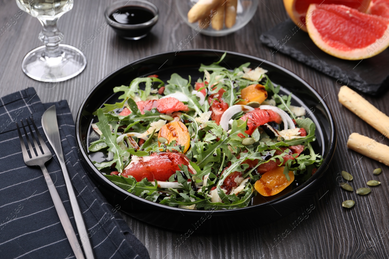 Photo of Tasty salad with arugula, cheese, grapefruit, vegetable and balsamic sauce on dark wooden table, closeup