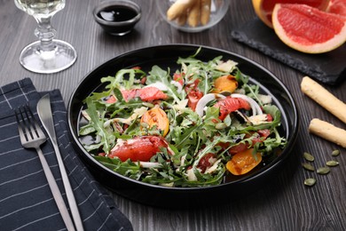 Photo of Tasty salad with arugula, cheese, grapefruit, vegetable and balsamic sauce on dark wooden table, closeup