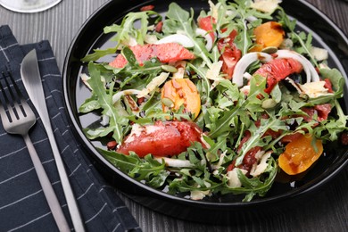 Photo of Tasty salad with arugula, cheese, grapefruit, vegetable and balsamic sauce on dark wooden table, closeup