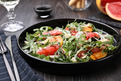 Photo of Tasty salad with arugula, cheese, grapefruit, vegetable and balsamic sauce on dark wooden table, closeup