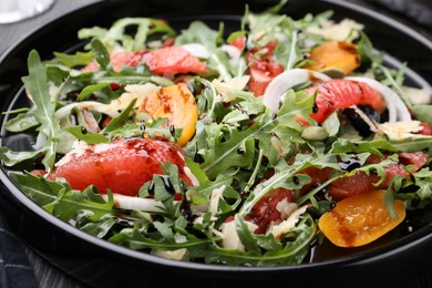 Photo of Tasty salad with arugula, cheese, grapefruit, vegetable and balsamic sauce on dark wooden table, closeup