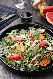 Photo of Tasty salad with arugula, cheese, grapefruit, vegetable and balsamic sauce on dark wooden table, closeup