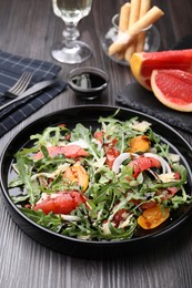Photo of Tasty salad with arugula, cheese, grapefruit, vegetable and balsamic sauce on dark wooden table, closeup