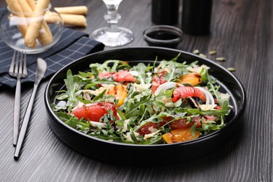 Photo of Tasty salad with arugula, cheese, grapefruit, vegetable and balsamic sauce on dark wooden table, closeup