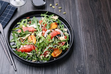 Photo of Tasty salad with arugula, cheese, grapefruit, vegetable and balsamic sauce on dark wooden table, closeup. Space for text