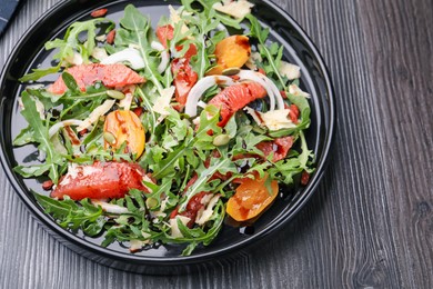 Photo of Tasty salad with arugula, cheese, grapefruit, vegetable and balsamic sauce on dark wooden table, above view