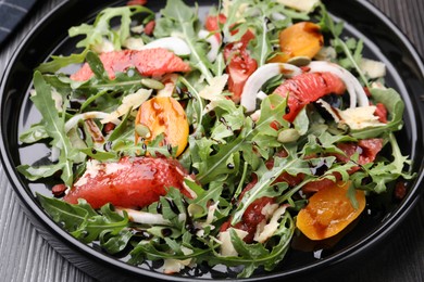 Photo of Tasty salad with arugula, cheese, grapefruit, vegetable and balsamic sauce on dark wooden table, closeup