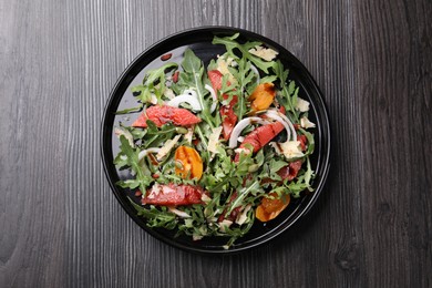 Photo of Tasty salad with arugula, cheese, grapefruit, vegetable and balsamic sauce on dark wooden table, top view