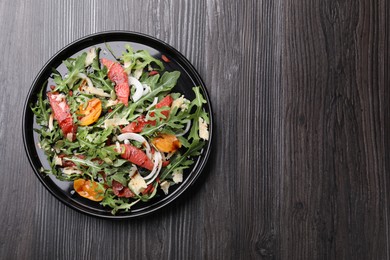 Photo of Tasty salad with arugula, cheese, grapefruit, vegetable and balsamic sauce on dark wooden table, top view. Space for text