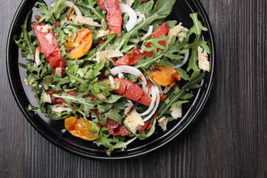 Photo of Tasty salad with arugula, cheese, grapefruit, vegetable and balsamic sauce on dark wooden table, top view