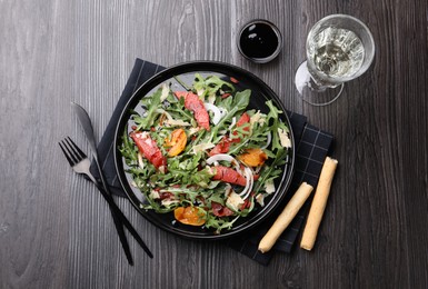 Photo of Tasty salad with arugula, cheese, grapefruit, vegetable and balsamic sauce served on dark wooden table, flat lay