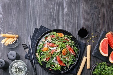 Photo of Tasty salad with arugula, cheese, grapefruit, vegetable and balsamic sauce served on dark wooden table, flat lay. Space for text